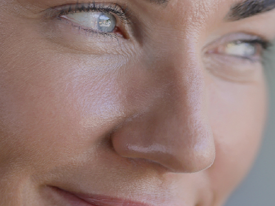 Close-up of a person's face, focusing on a portion of their nose, mouth, and eyes. The lighting highlights their smooth skin and blue eyes, with a slight smile visible.