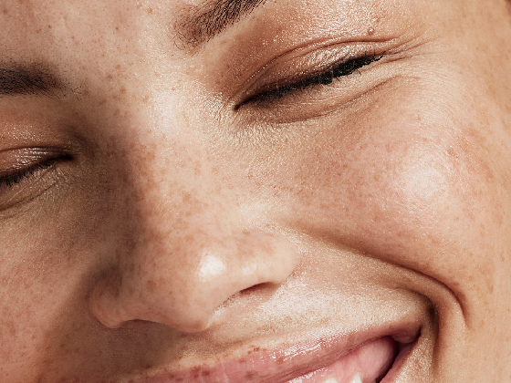Close-up of a person's face with closed eyes and a smile, highlighting clear skin with freckles, reflecting the benefits of green chemistry in skincare.