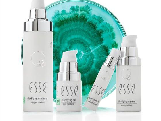 menu_clarifying A product display featuring four white skincare bottles labeled "esse": a clarifying cleanser, clarifying oil, an eye product, and a clarifying serum. The items are arranged in front of a teal and white marbled background.