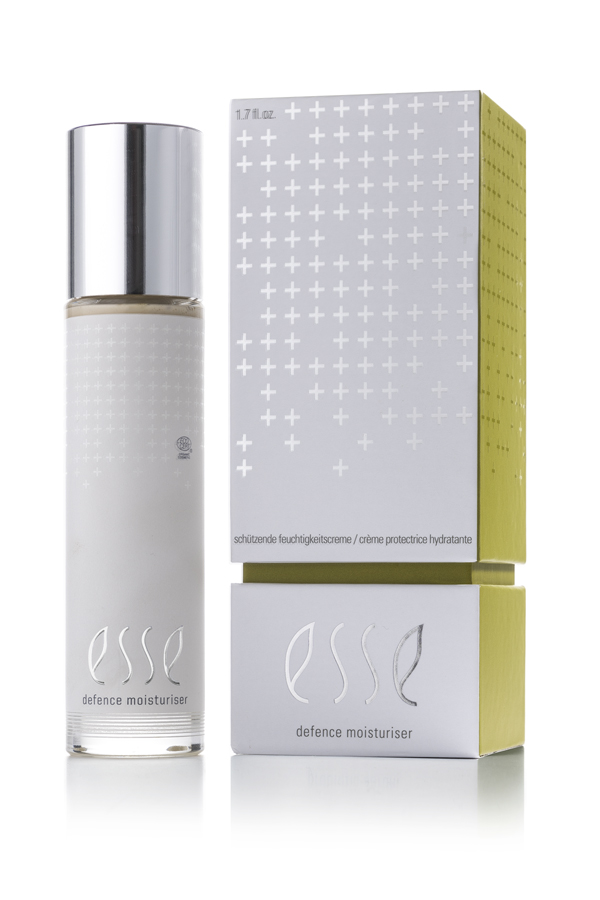 A bottle of Esse Defence Moisturiser with a silver cap sits beside its coordinating silver and yellow box, both featuring minimalist modern design and the product name in lowercase letters.