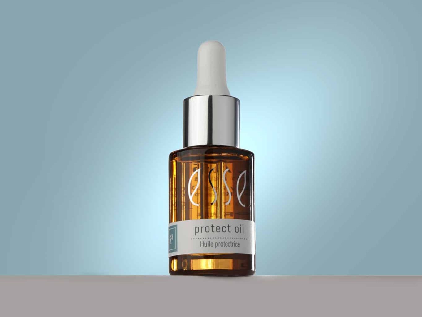 thumbnail_Protect_Oil_Insta_Crop A small amber glass bottle of Esse Protect Oil stands on a neutral surface against a gradient pale blue background. The bottle, with a silver and white dropper cap, features the brand name "Esse" and a label indicating it is protective oil.