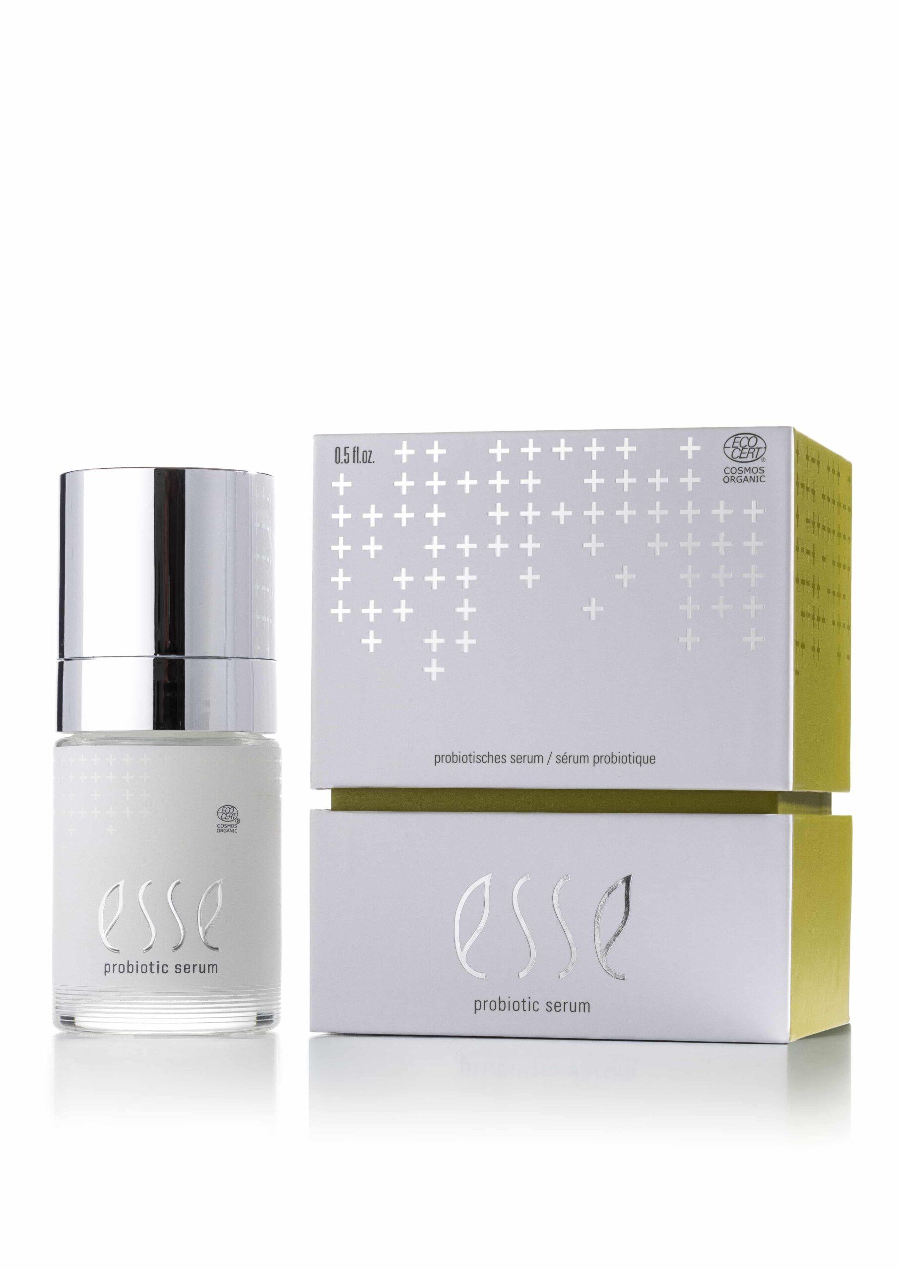 A bottle of Esse Probiotic Serum with a silver cap stands beside its white and yellow box, which features plus sign patterns and the product name.