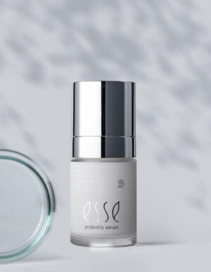 A bottle of Import placeholder for 56489 with a shiny silver cap stands upright on a light gray surface, soft shadows cast around it and a blurred jar lid in the background.