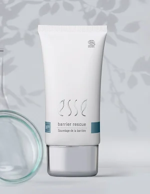 A white tube of Import placeholder for 57617 skincare cream stands upright, with subtle shadows and botanical patterns in the background. A glass container is partially visible on the left side.